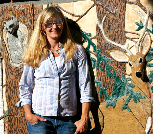 IClay sculptor Sherry Bennett poses in front of part of the
wall outside her house that shes overlaid with nature
scenes, including the full-relief heads of a raccoon and a deer.
Westside Pioneer photo