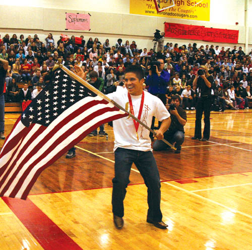 Wearing his Olympic gold medal and waving the American flag he carried into the Coronado High gymasium, 06 
graduate Henry Cejudo grins at family members while students cheer and media members photograph him Oct. 28 during a school assembly in his honor.
Westside Pioneer photo